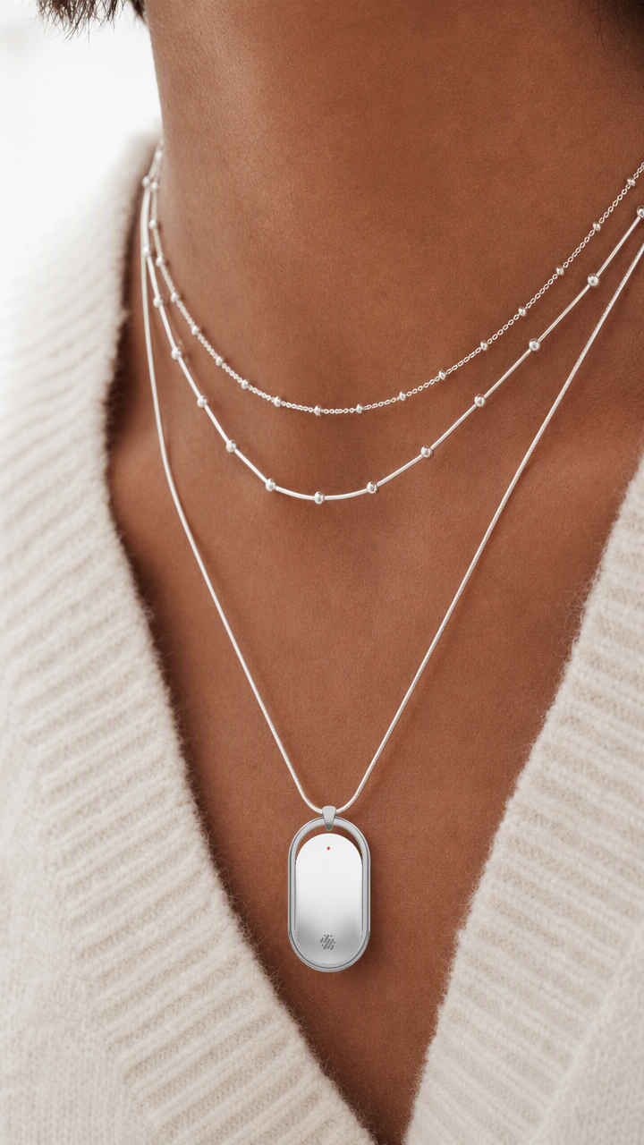 NUVA worn as a pendant with layered necklaces and a white cardigan.